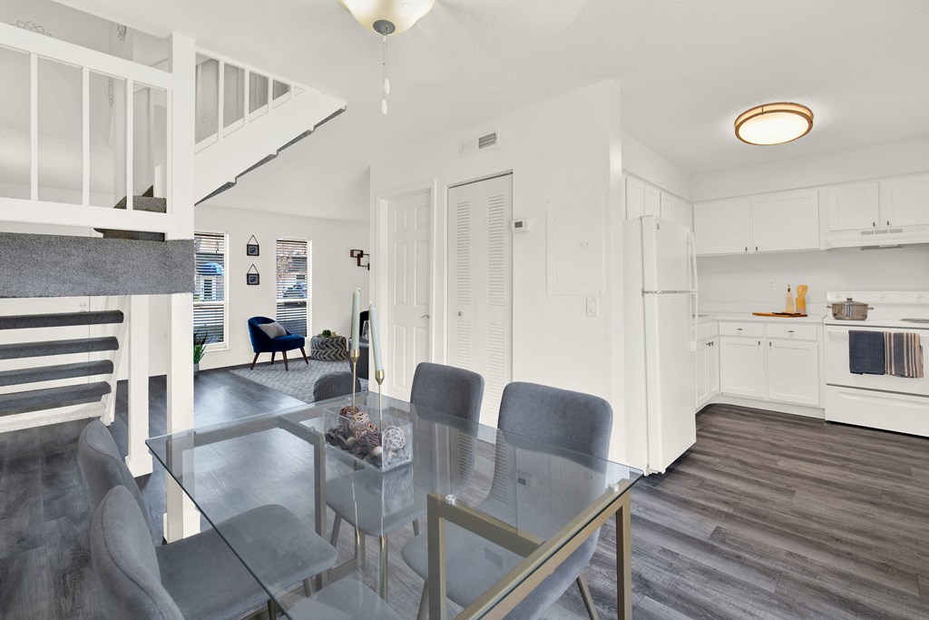 A modern kitchen with a glass dining table and grey chairs.