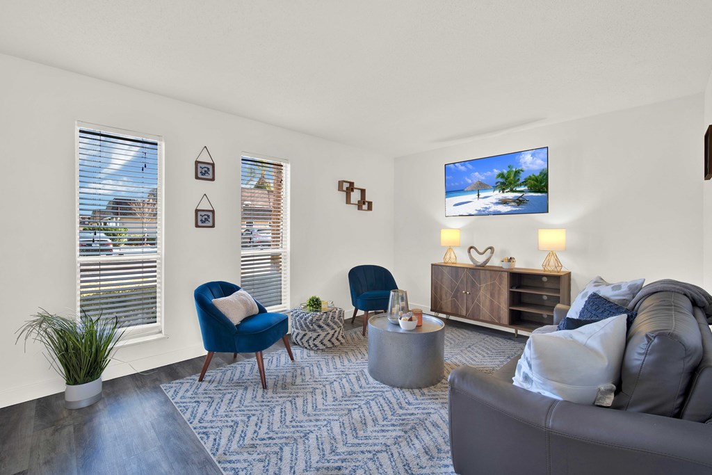 A living room with a grey couch, blue chairs, and a TV displaying a beach scene.
