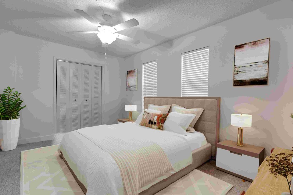 A bedroom with a large bed, a ceiling fan, and a potted plant.