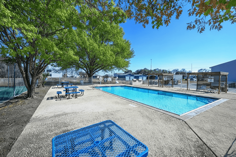 A blue poolside chair is in the foreground of a sunny pool area at Ranch at 1856 Apartments, San Marcos, TX