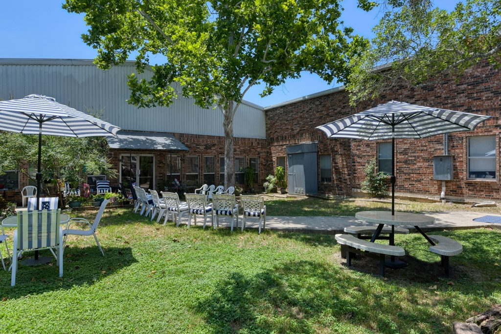 A patio with chairs and umbrellas is set in front of a brick building.
