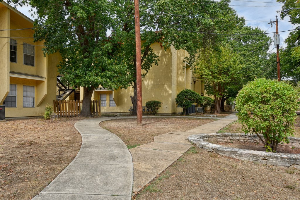 a sidewalk in front of a yellow building with trees  at Mayfield Gardens, San Antonio, 78211