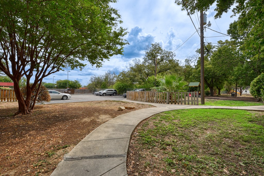 a sidewalk in a park with trees and a parking lot  at Mayfield Gardens, San Antonio, 78211