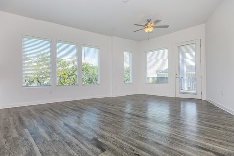 A room with a ceiling fan and large windows.