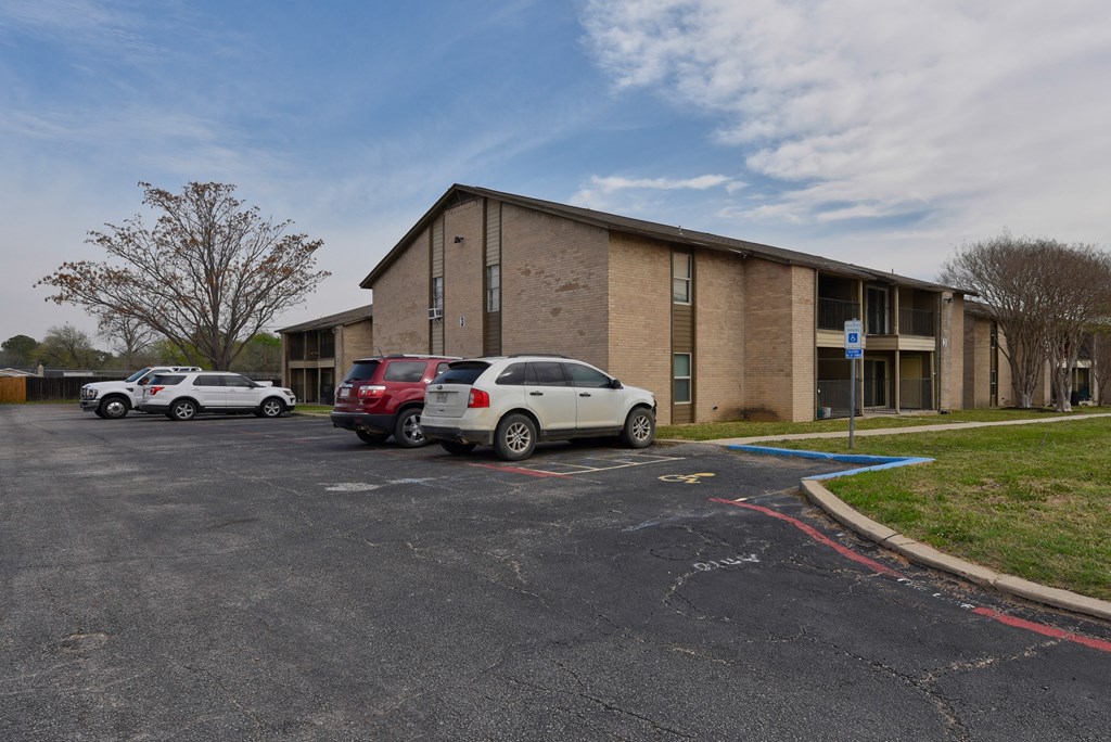 a parking lot with cars in front of a brick building at Eagle View Apartments, Pleasanton, Texas