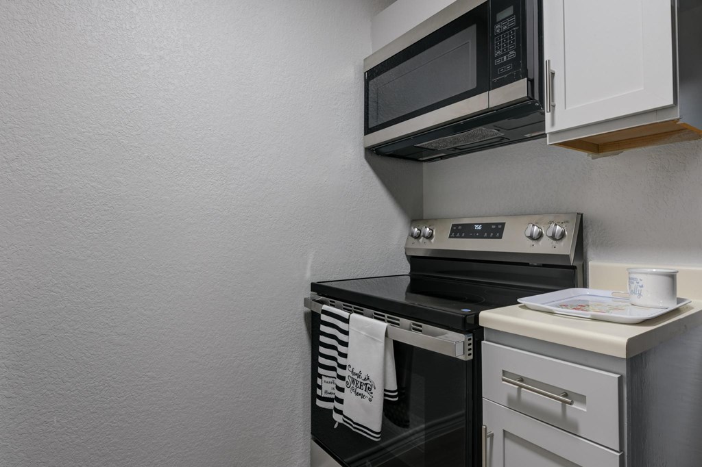 A black microwave is mounted above a stove in a kitchen.