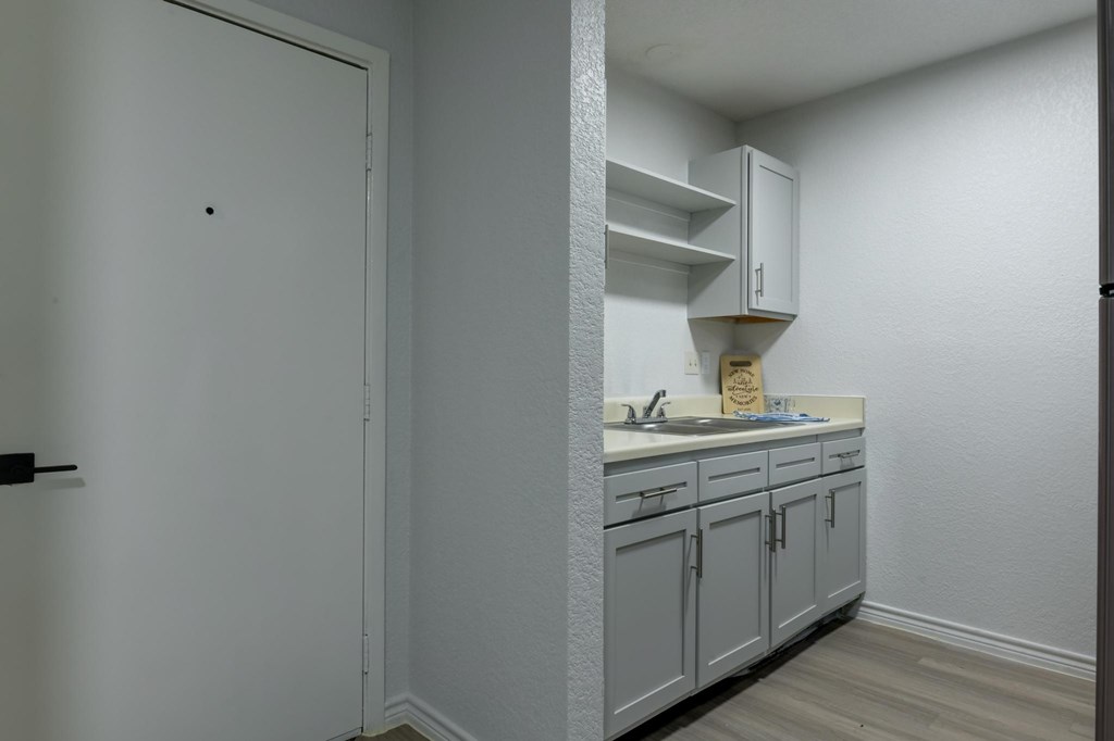 A white door is on the left of a kitchen with grey cabinets.