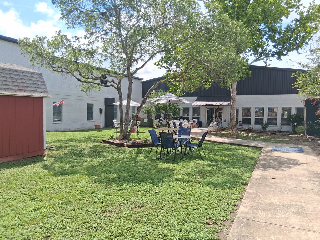 A white building with a red door and a tree in front.