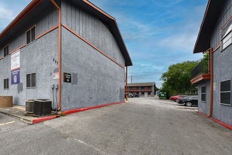 a parking lot in front of a gray building with a red curb at The Crossings at Montrose Apartments, San Antonio
