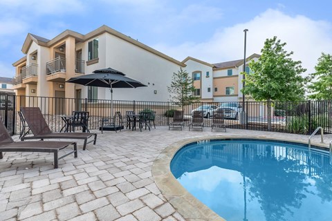 A pool surrounded by a patio with chairs and an umbrella.