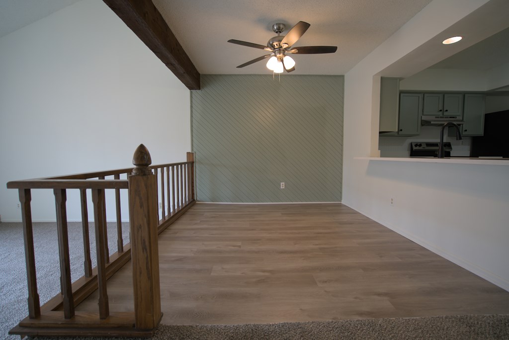 A room with a ceiling fan and a wooden railing.