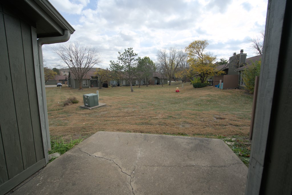 A backyard with a concrete slab in the foreground and a mailbox in the middle.