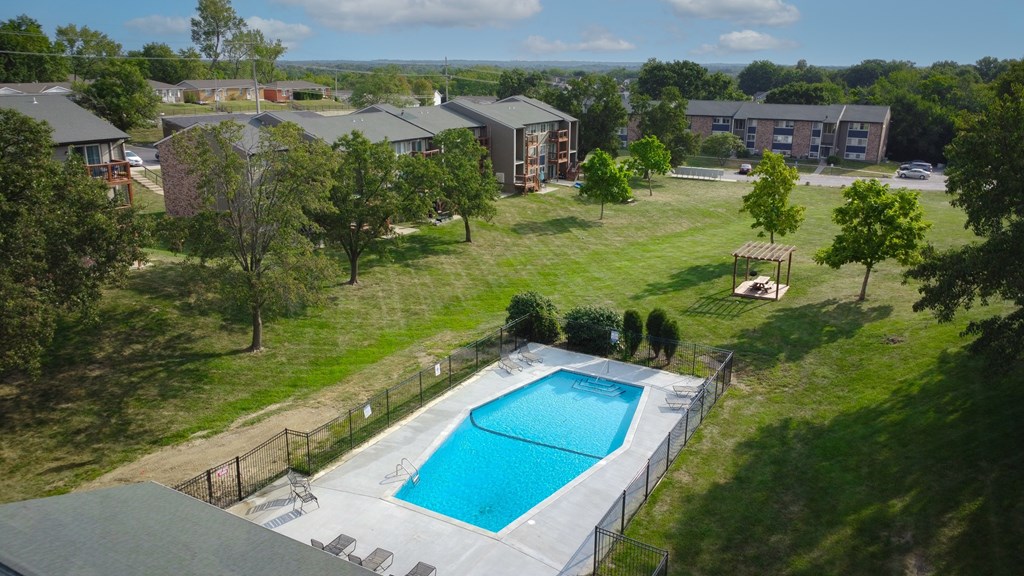 A swimming pool surrounded by a fence and trees in a residential area.