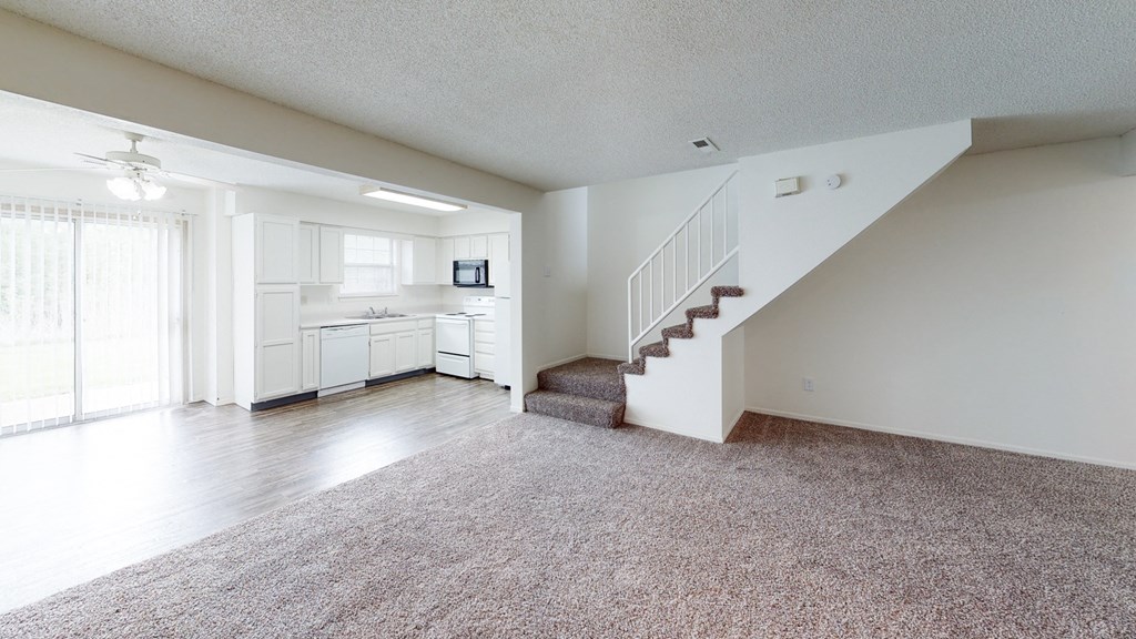 an empty living room with a staircase and a kitchen