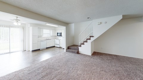an empty living room with a staircase and a kitchen