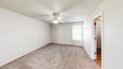 a spacious living room with carpet and a ceiling fan