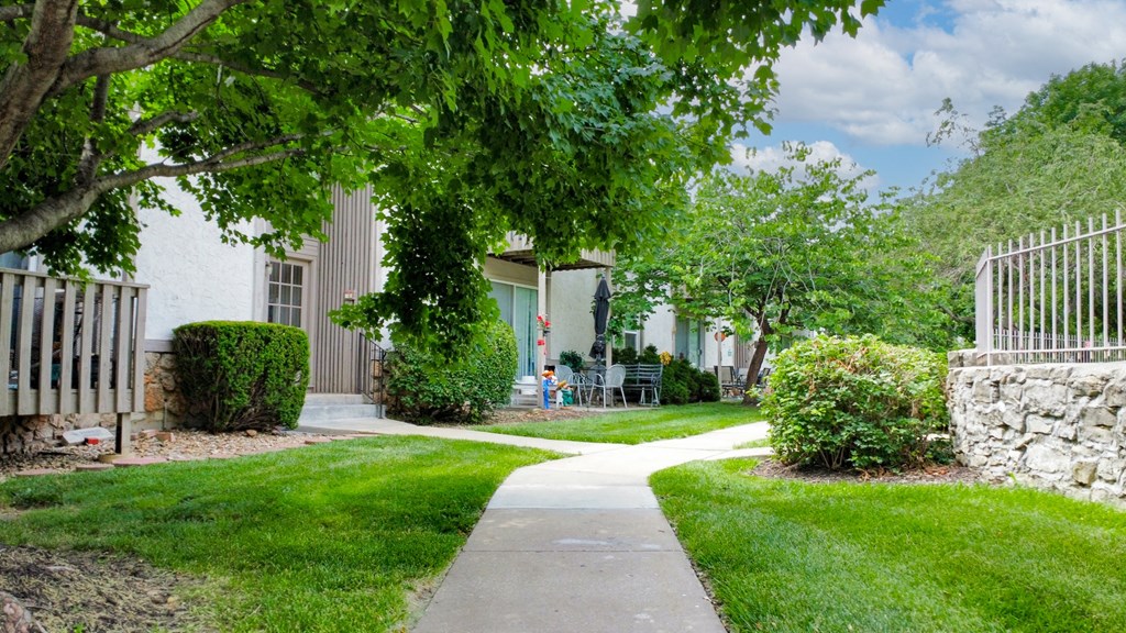 a sidewalk in front of a house with green grass and trees