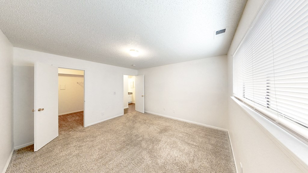 a spacious living room with a large window and a carpeted floor