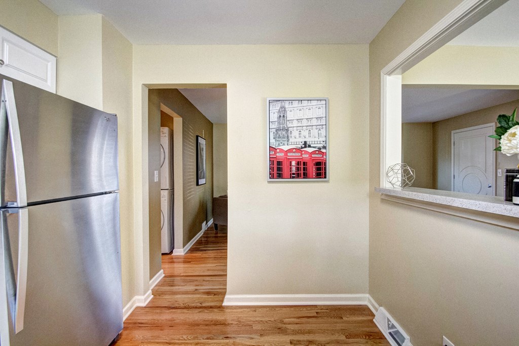 A kitchen with a refrigerator on the left and a painting of a building on the wall.