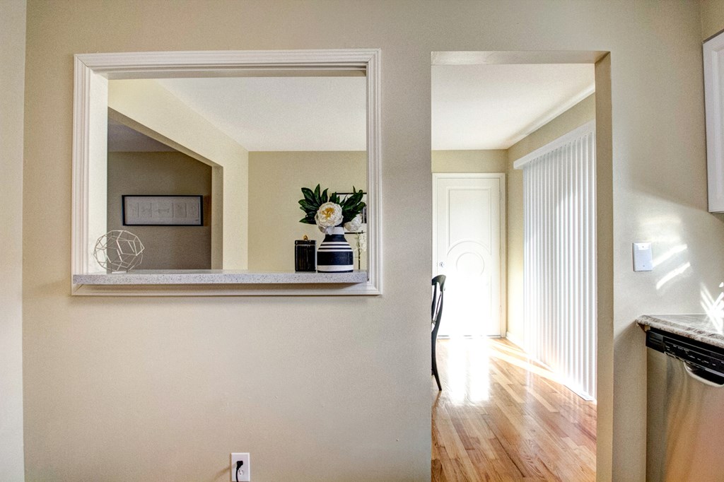 A white framed mirror hangs on a wall above a wooden floor.