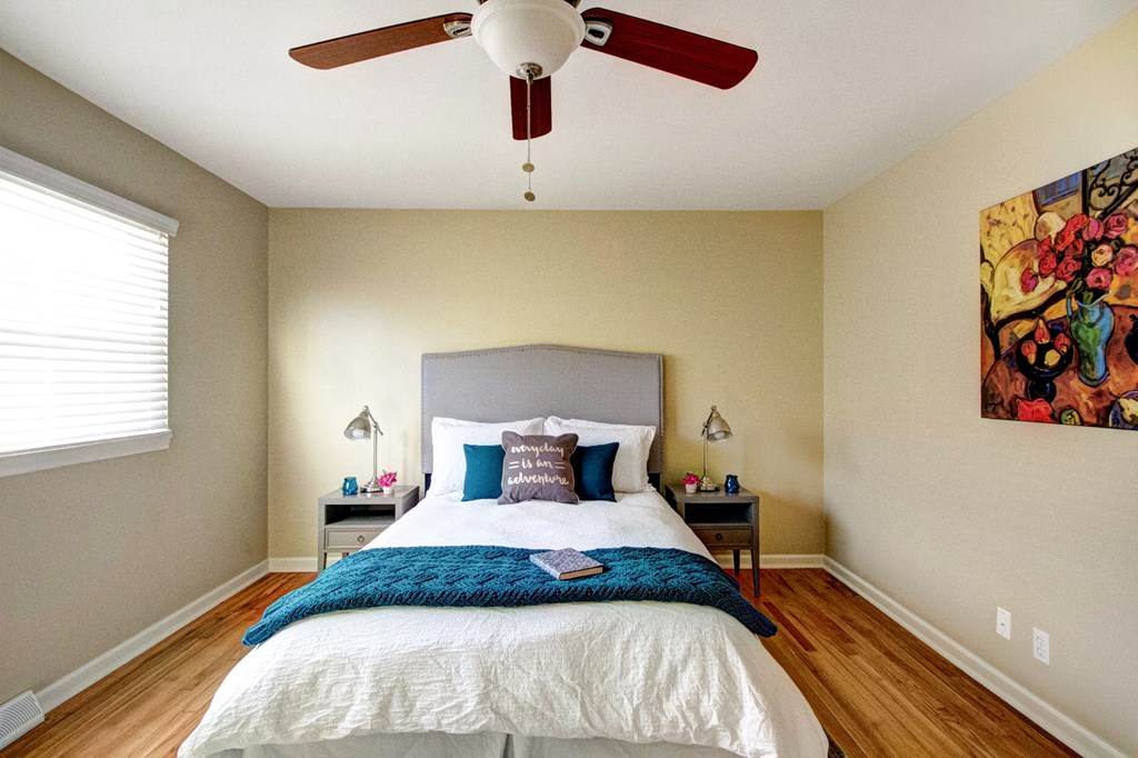 A bedroom with a bed, two lamps, and a ceiling fan.