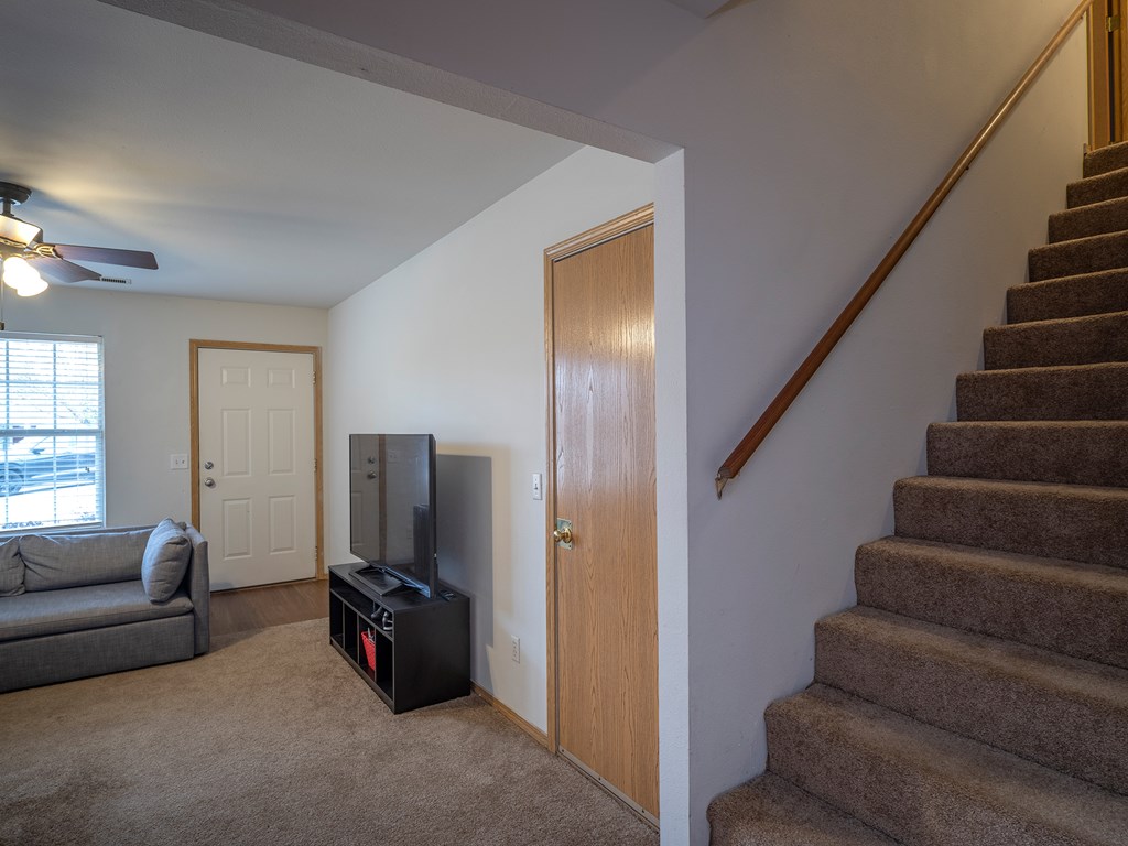 A living room with a grey couch, a television, and a staircase.