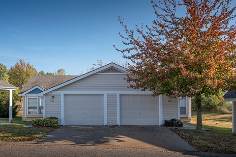 A house with a white garage door is in front of a tree with red leaves.