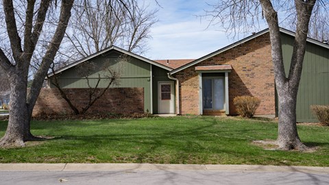 A house with a green roof and a brick exterior is surrounded by trees.