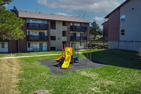 A playground with a yellow slide in front of a brick apartment building.