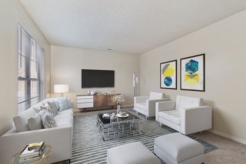 A living room with a grey sofa, a white armchair, a grey ottoman, a glass coffee table, a television, and two framed pictures on the wall.