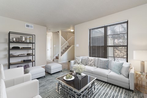 A living room with a white couch, a coffee table, and a staircase in the background.