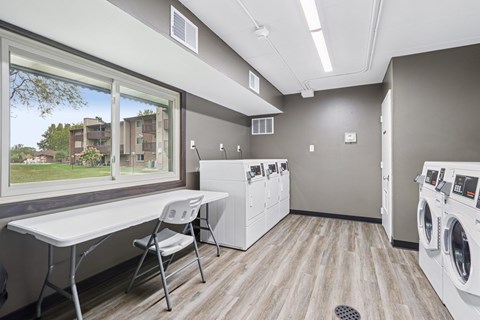 A laundry room with a washer and dryer, a table and a chair.