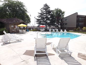 A pool with chairs around it and a building in the background.