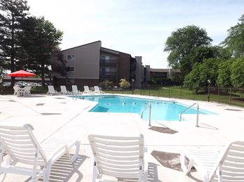 A pool surrounded by white chairs and a building in the background.