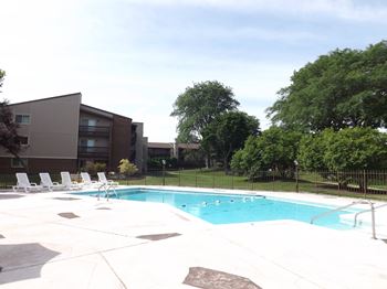 A swimming pool surrounded by a concrete patio and a building in the background.