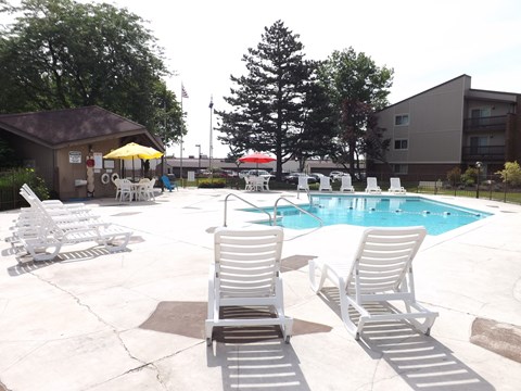 A pool with chairs around it and a building in the background.
