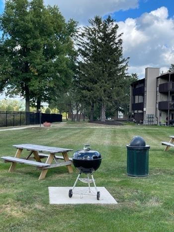 A picnic table and a grill are on a white mat in a grassy area.