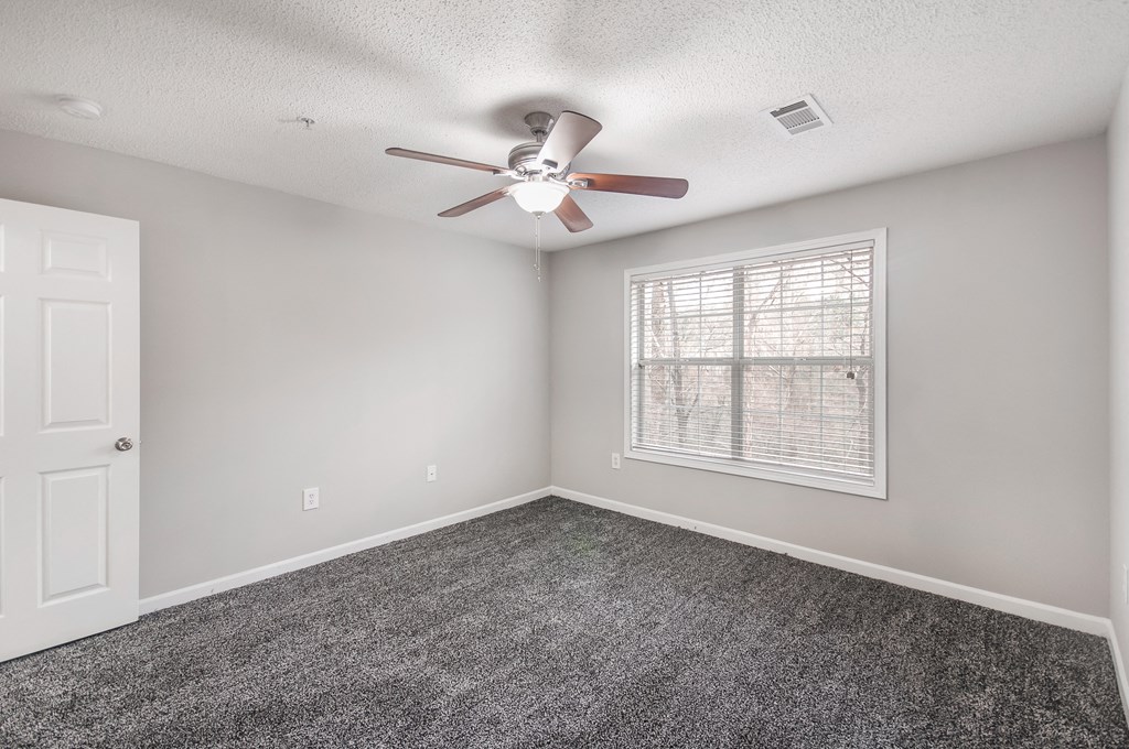 an empty bedroom with a ceiling fan and a window
