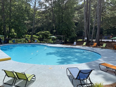 a swimming pool with chaise lounge chairs and trees in the background