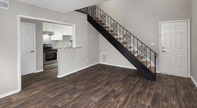 an empty living room with a staircase and a kitchen