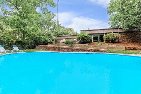 A swimming pool surrounded by trees and a building in the background.
