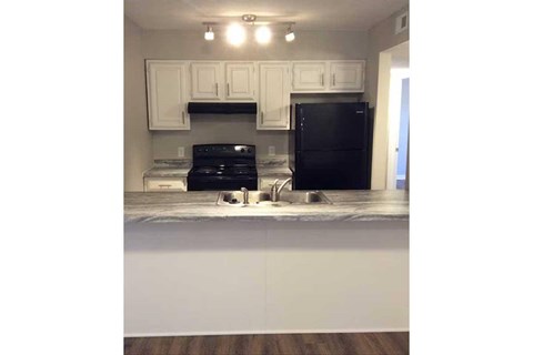 A black refrigerator sits in a kitchen with white cabinets.