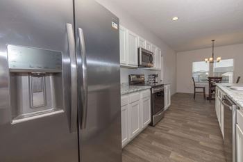 A modern kitchen with a stainless steel refrigerator and wooden flooring.