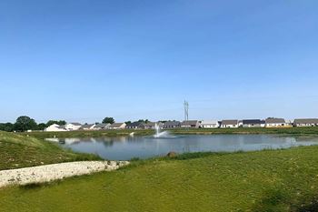 A body of water surrounded by grass and houses in the distance.