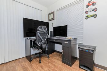 A black computer desk with a chair and a monitor in a room.