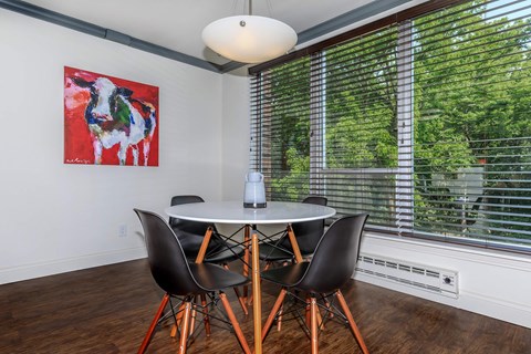 A dining room with a table and chairs and a painting on the wall.