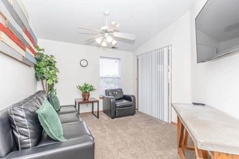 A living room with a grey couch, a black armchair, a wooden table, and a television.