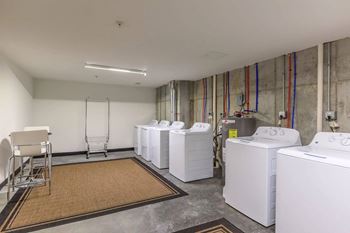A laundry room with a washer and dryer on the right and a chair and rack on the left.