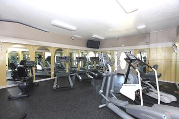 A gym with a variety of equipment including treadmills, elliptical machines, and weights.