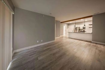 A room with wooden flooring and a kitchen area in the background.